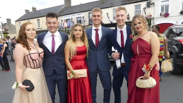 Un grupo de personas en ropa formal posan frente al paisaje urbano en el campus del Kilkenny College.