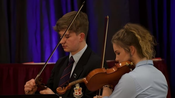 Dos estudiantes del Kilkenny College tocan el violín y el arco en un escenario con cortina roja.