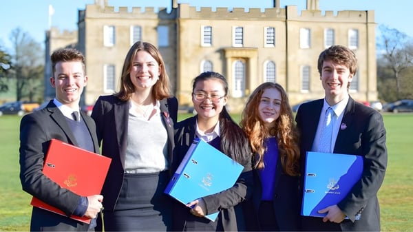 Cinco jóvenes adultos están de pie con ropa formal frente a un edificio histórico en el campus de la Kimbolton School.