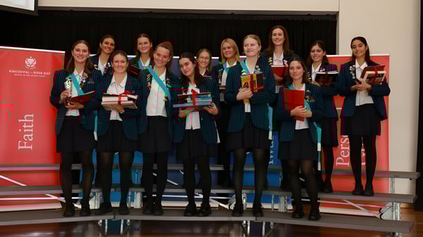 Un grupo de egresadas de Kincoppal-Rose Bay está frente a un fondo rojo con certificados en la mano.