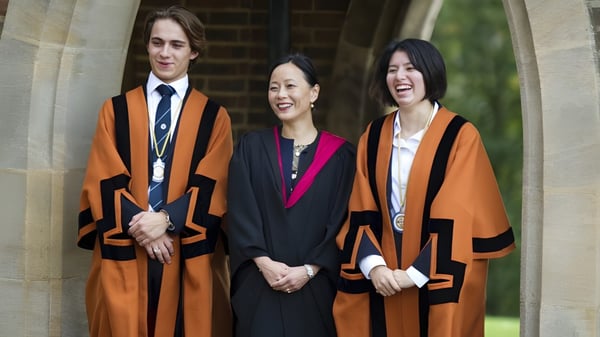 Tres personas en togas académicas están de pie frente a un arco de piedra en el terreno de la King Edward's Witley School.