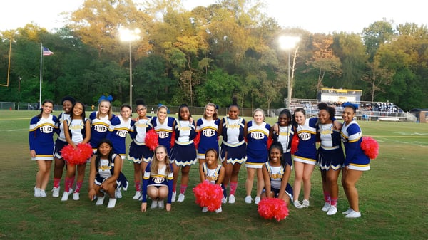 Un grupo de animadoras en uniformes coloridos posan juntas en el campo de deportes de la King George Secondary School.