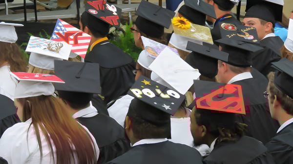 Los graduados del King William's College llevan togas y birretes negros en una ceremonia de graduación al aire libre.