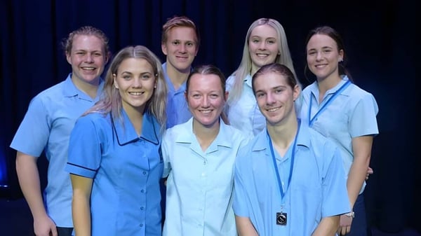 Un grupo de alumnas y alumnos de la Kingaroy State High School lleva uniformes azules y está frente a un fondo oscuro.
