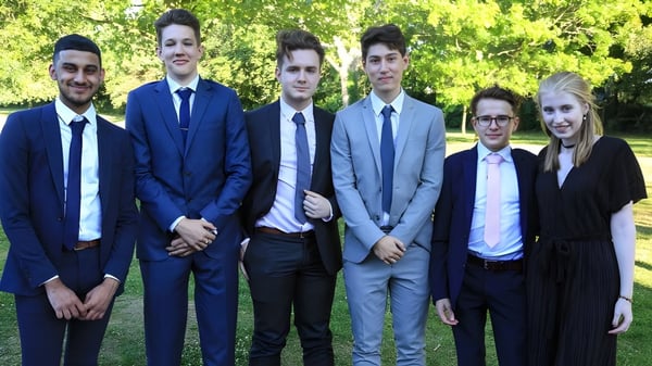 Un grupo de seis personas vestidas formalmente está reunido en el parque en el terreno de la Kingham Hill School.