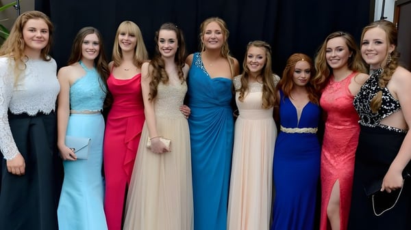 Un grupo de jóvenes mujeres en vestidos de fiesta posan juntas frente a un fondo oscuro en el campus de King's Bruton.