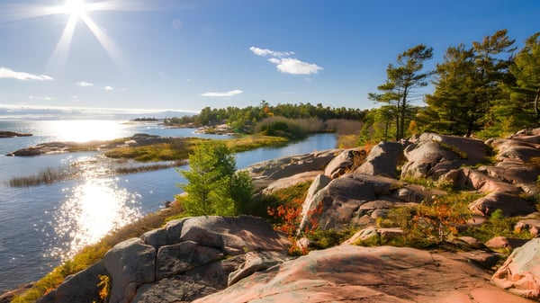 Un lago tranquilo con una línea de costa rocosa y pinos en el paisaje cerca de la King’s-Edgehill School.