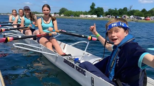 Un grupo de alumnas y alumnos de King's Ely está sentado en un pequeño bote en un cuerpo de agua rodeado de árboles.