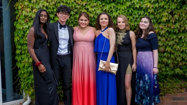 Un grupo de cinco personas en ropa formal está frente a una pared cubierta de hiedra en el terreno de la King's School.