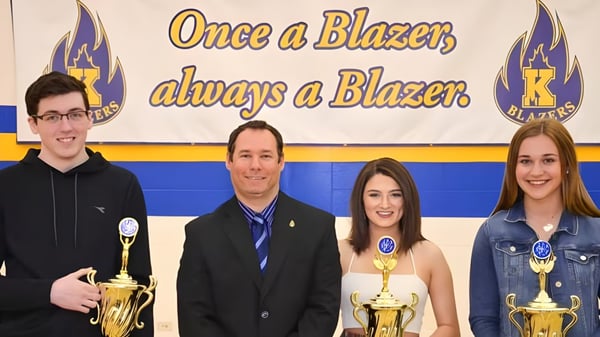 Cuatro alumnos de la Kinkora Regional High School posan frente a un banner con trofeos.