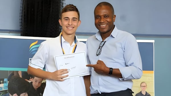 Un estudiante de Kinross College sostiene un certificado y está al lado de un hombre mayor.