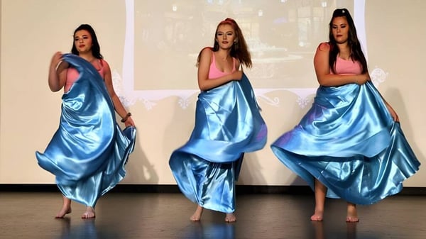 Tres alumnas de Kinross College llevan largos vestidos de satén azules en una habitación con fondo blanco.