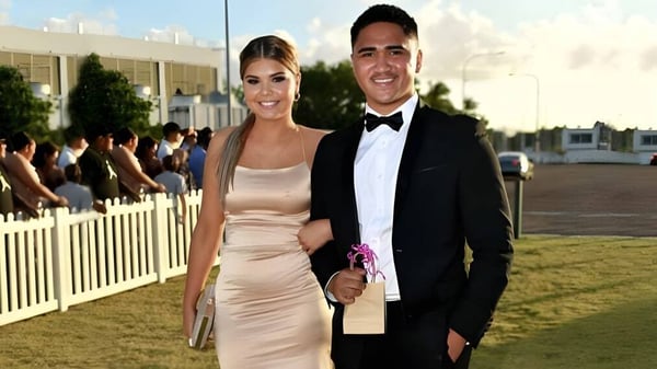 Una pareja bien vestida está de pie en una pradera frente a una multitud en el terreno de la Kirwan State High School.