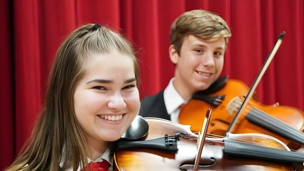 Estudiantes de la Kirwan State High School tocan juntos el violonchelo en un escenario frente a una cortina roja.