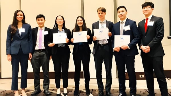 Estudiantes de la Kitsilano Secondary School están vestidos formalmente con certificados frente a un fondo neutro.