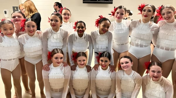 Un grupo de jóvenes bailarinas posa juntas en trajes blancos y beige en el estudio de danza de la Kokomo Center Township Consolidated School Corporation.
