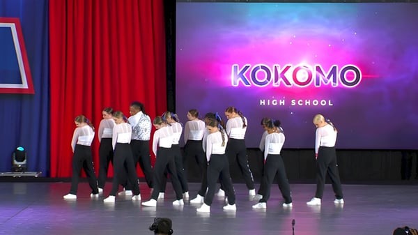 Estudiantes de la Kokomo High School se presentan en un escenario con un gran nombre de la escuela de fondo.