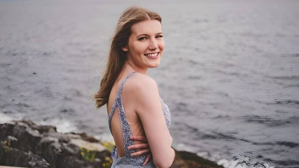 Una joven sonríe frente a un paisaje rocoso con cielo nublado en el terreno de la Kwalikum Secondary School.