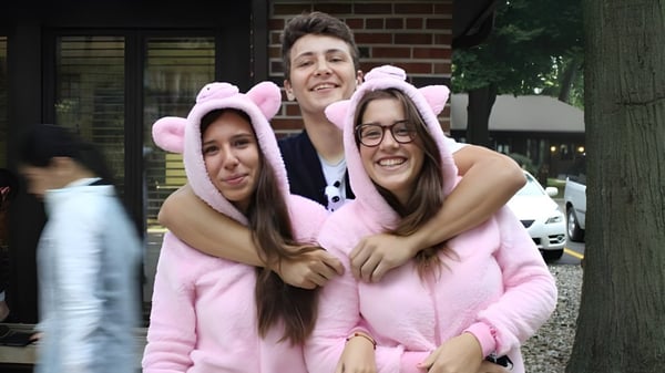 Tres estudiantes de la La Lumiere School se abrazan frente a un edificio de ladrillo y sonríen.