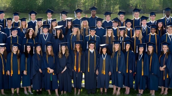 Graduados de la La Lumiere School están de pie en ropa académica en un campo.