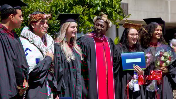 Un grupo de egresadas y egresados de La Salle Secondary School está al aire libre frente a un fondo verde con vestimenta académica.