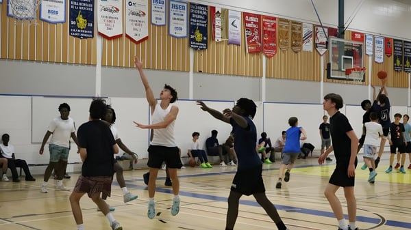 Estudiantes de la École secondaire publique L'Académie de la Seigneurie jugando baloncesto en la cancha con pancartas de fondo.