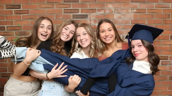 Un grupo de jóvenes mujeres en vestimenta de graduación posando frente a una pared de ladrillo en el terreno de la École secondaire publique L'Académie de la Seigneurie.