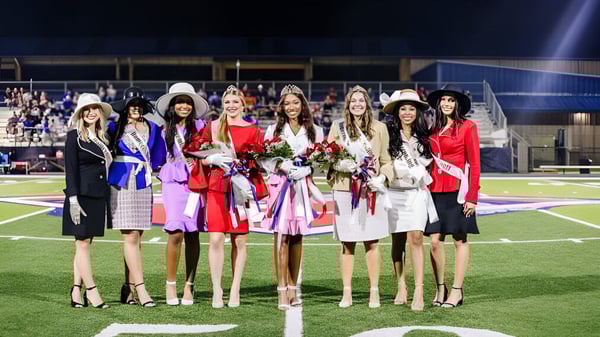 Un grupo de estudiantes de Lafayette Christian Academy está de pie por la noche en el campo de fútbol sosteniendo ramos de flores en una fiesta.