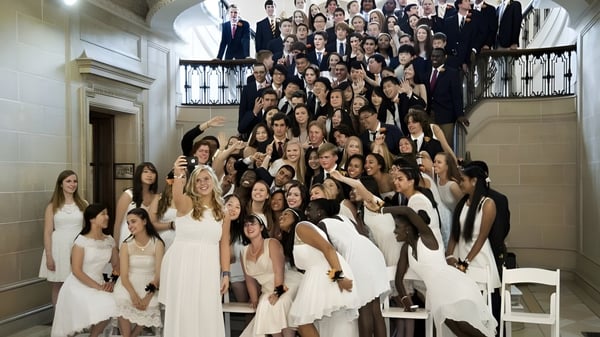 Un gran grupo de personas vestidas de manera formal se reúne en el aula representativa de la Lake Forest Academy.
