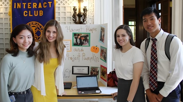 Cuatro estudiantes de la Lake Forest Academy están frente a una pantalla con la inscripción Interact Club y una laptop.