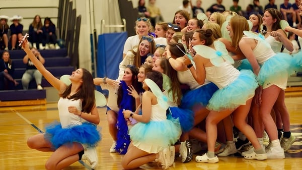 Alumnas de la Lake George Junior-Senior High School en coloridos trajes de baile posan juntas en el escenario.
