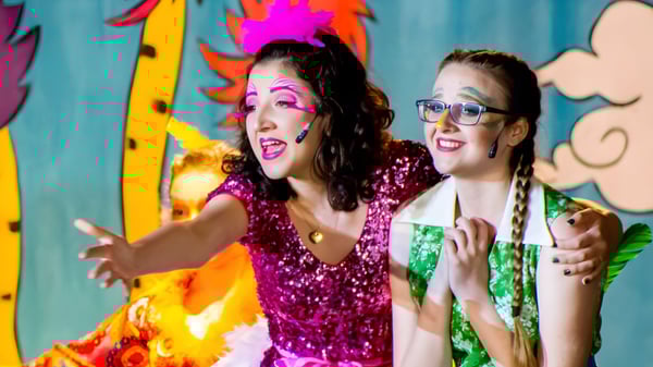 Dos mujeres en trajes coloridos y brillantes frente a un fondo abstracto colorido en el campus de la Lake Mary Preparatory School.