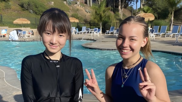 Dos estudiantes de la Lake Tahoe Preparatory School muestran signos de paz sonriendo frente a una piscina con palmeras.