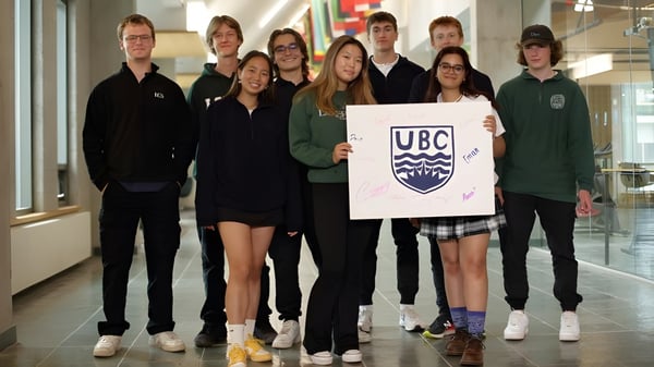 Un grupo de estudiantes de Lakefield College School está junto en un edificio escolar sosteniendo un cartel con el logo de UBC.