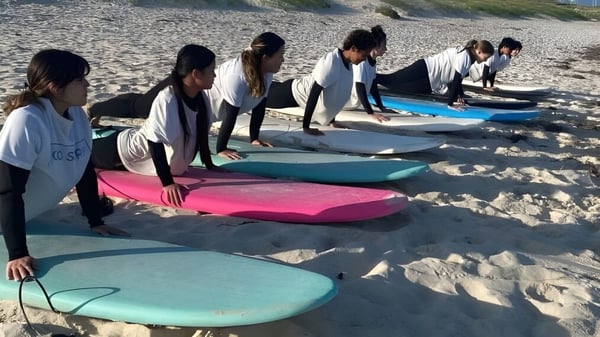 Un grupo de estudiantes de la Lakeland Senior High School está en trajes de neopreno en la playa con coloridas tablas de surf.