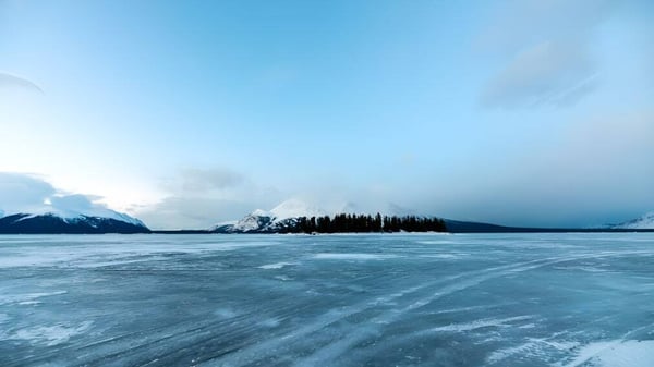 Un lago congelado con montañas cubiertas de nieve y pinos bajo un cielo nublado cerca de la Lakes District Secondary School.