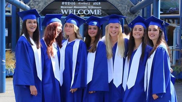 Un grupo de estudiantes de la Lambrick Park Secondary School celebra frente a un cartel de bienvenida su graduación en togas azules.