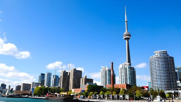 Un moderno horizonte urbano con altos rascacielos y una torre de televisión frente a un cielo azul cerca del L'Amoreaux Collegiate Institute.
