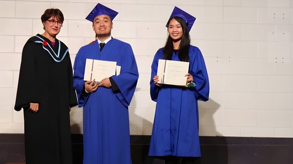 Tres graduados del L'Amoreaux Collegiate Institute posan con sus diplomas frente a una pared blanca.