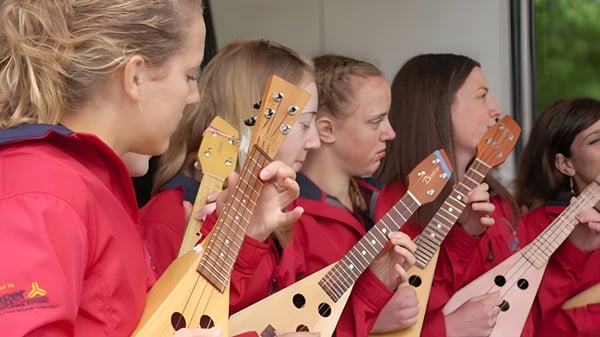 Un grupo de estudiantes de la Langley Fine Arts School está en uniformes rojos con varias guitarras en una sala de ensayo.