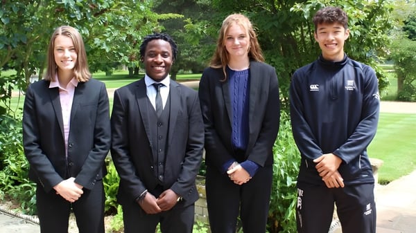 Cuatro personas vestidas de forma formal están juntas en el verde del campus de la Langley School.