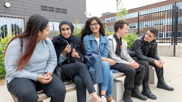 Estudiantes sentados en un banco frente a un edificio de diseño moderno en el campus de la Langley Secondary School.