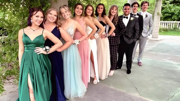 Un grupo de personas elegantemente vestidas se encuentra juntas en el área verde exterior de Lansing Catholic High School.