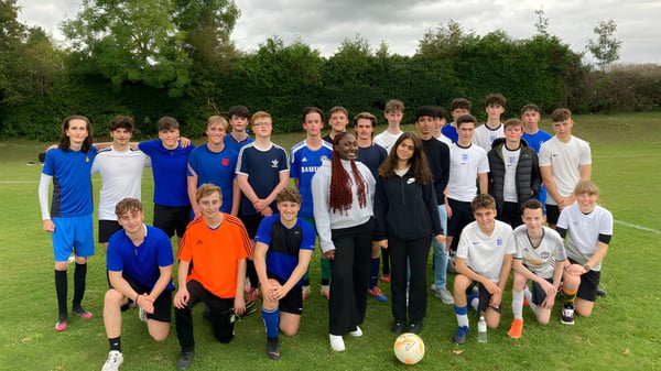 Un grupo de alumnas y alumnos está en una pradera con árboles al fondo en el terreno de la Larkmead School.