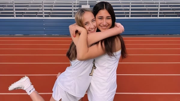 Dos alumnas del Las Virgenes Unified School District se abrazan en una pista roja frente a las gradas del estadio.