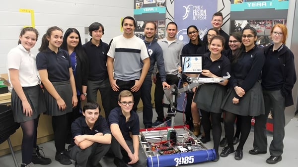 Un grupo de estudiantes posa en un aula de taller de LaSalle Community Comprehensive High School con varios equipos de fondo.