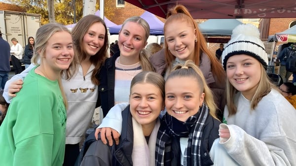 Un grupo de jóvenes estudiantes se encuentra en el campus de Launceston College frente a coloridas hojas de otoño.