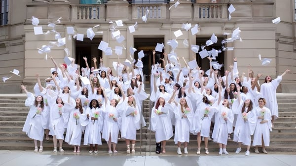 Un grupo de estudiantes de la Laurel School en túnicas blancas se reúne con banderas blancas en una escalera de un gran edificio.