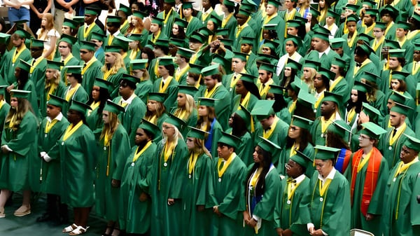 Un gran grupo de graduados de la Laurens Academy en togas verdes y amarillas posan juntos para una foto grupal.