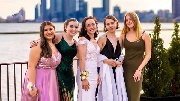 Un grupo de cinco alumnas de la Lawrence Academy posan frente a un horizonte urbano con altos edificios.